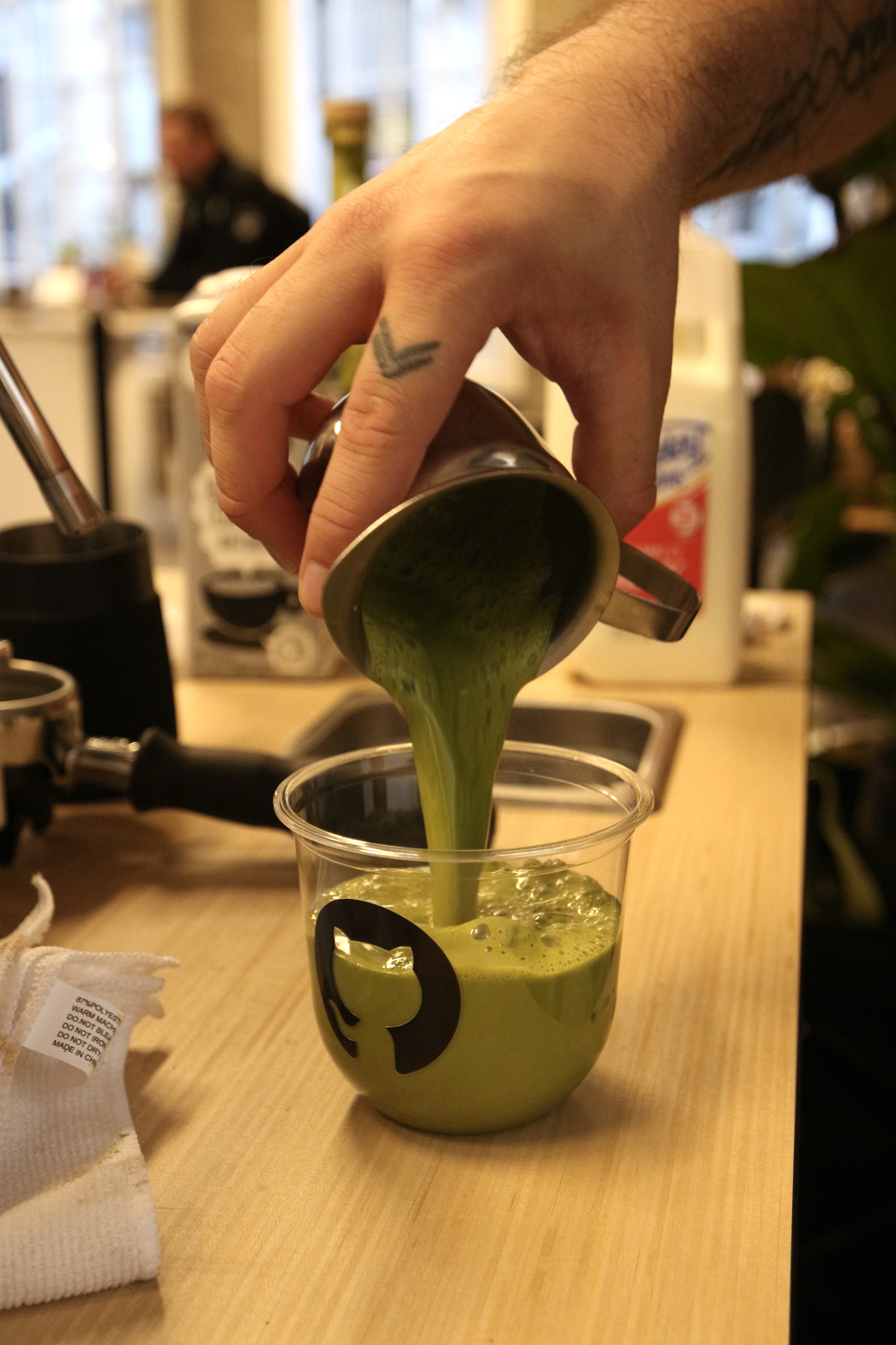 Barista pouring ceremonial matcha into a GitHub-branded branded cup at the Fez Coffee espresso bar.