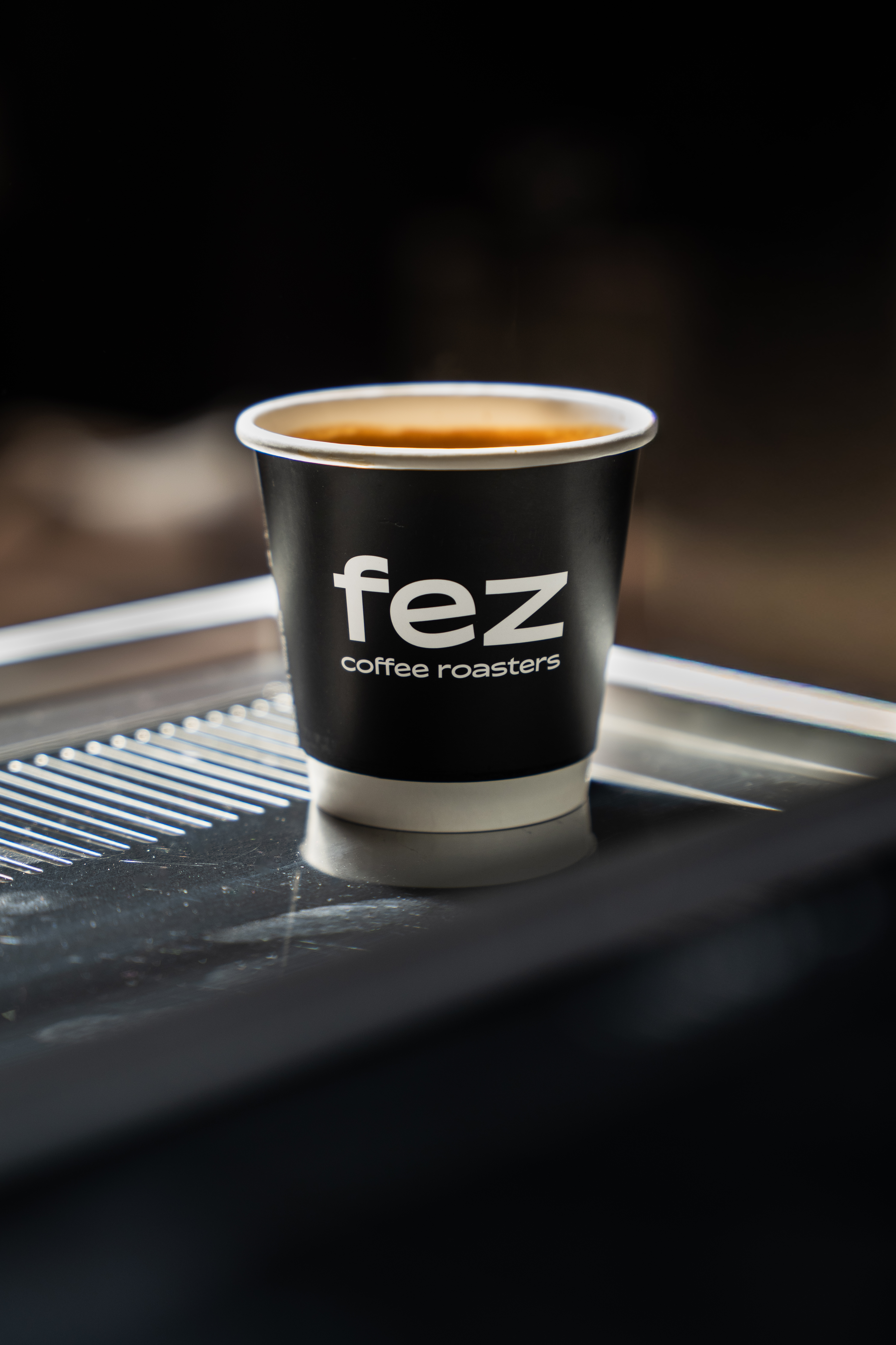 Fez Coffee paper espresso cup sitting on the drip tray of a commercial espresso machine.