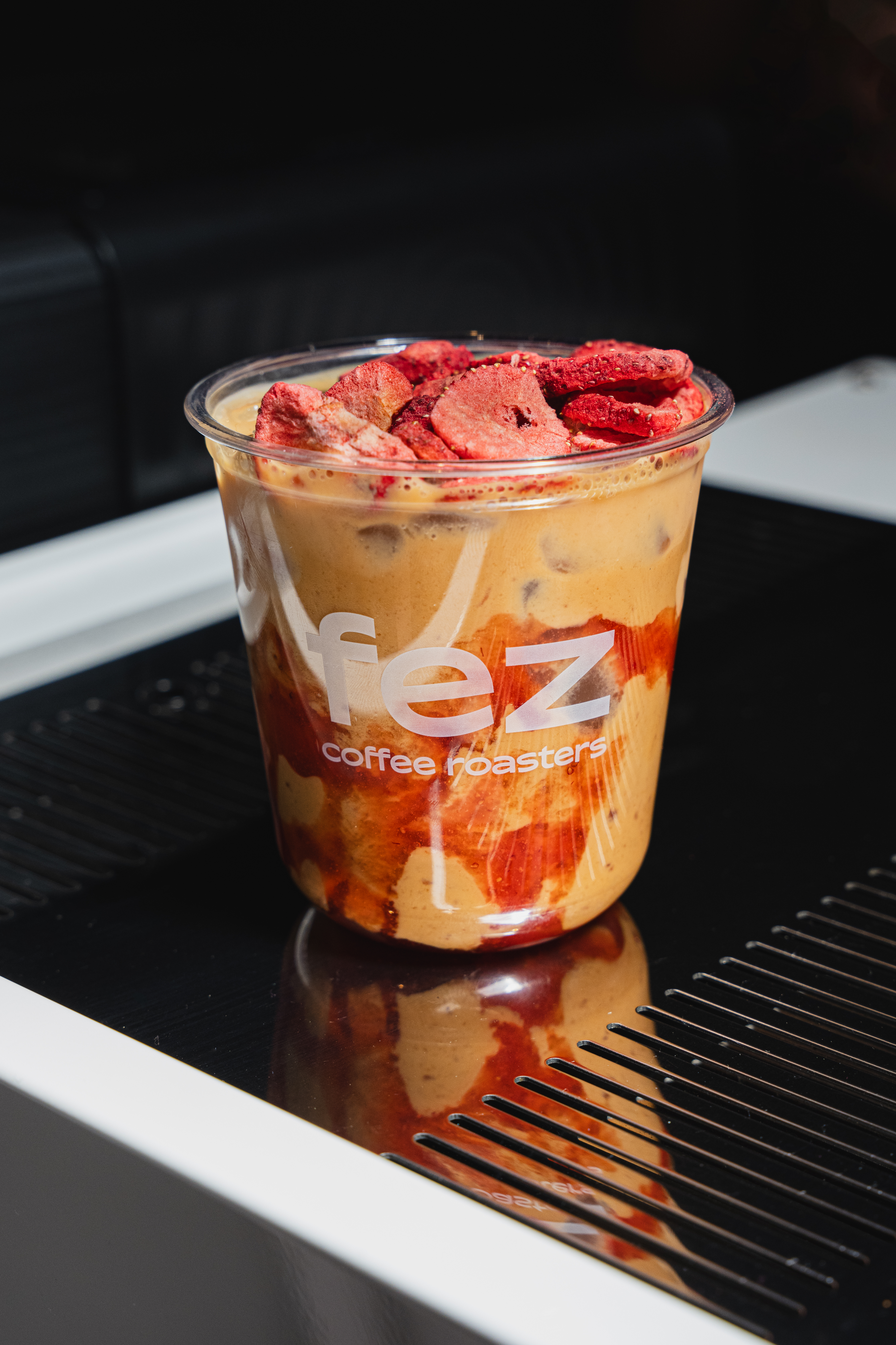 Fez Coffee iced latte with freeze-dried strawberries on top, sitting on an espresso machine drip tray.